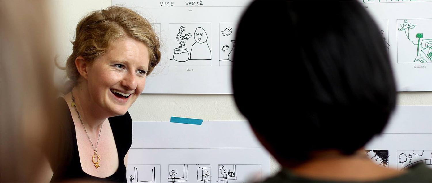 smiling blonde woman with drawings on wall behind herl